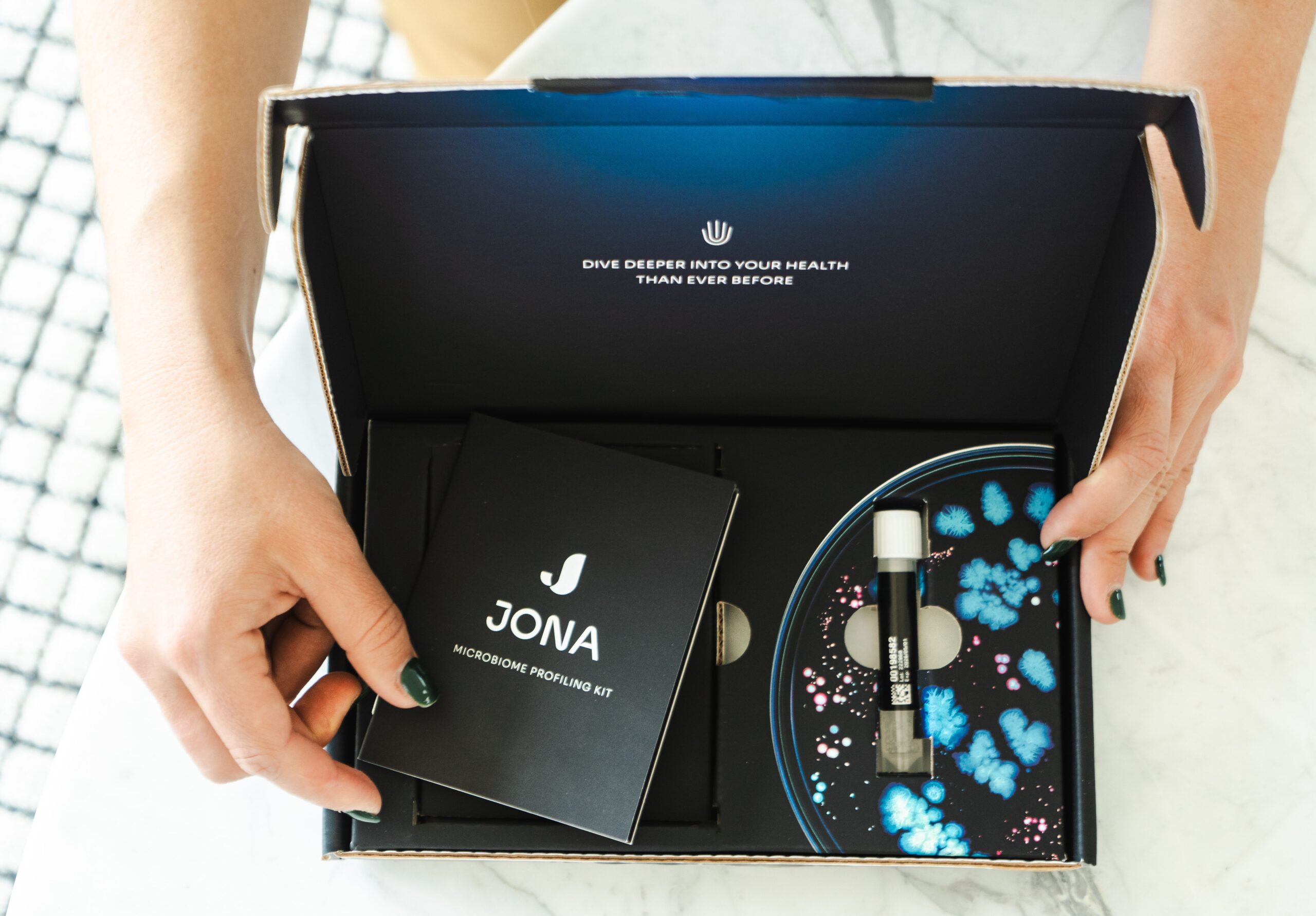 A person opens a gut health test kit on a marble table, revealing a comprehensive guide to nurturing microbiome balance alongside a test tube for sample collection.