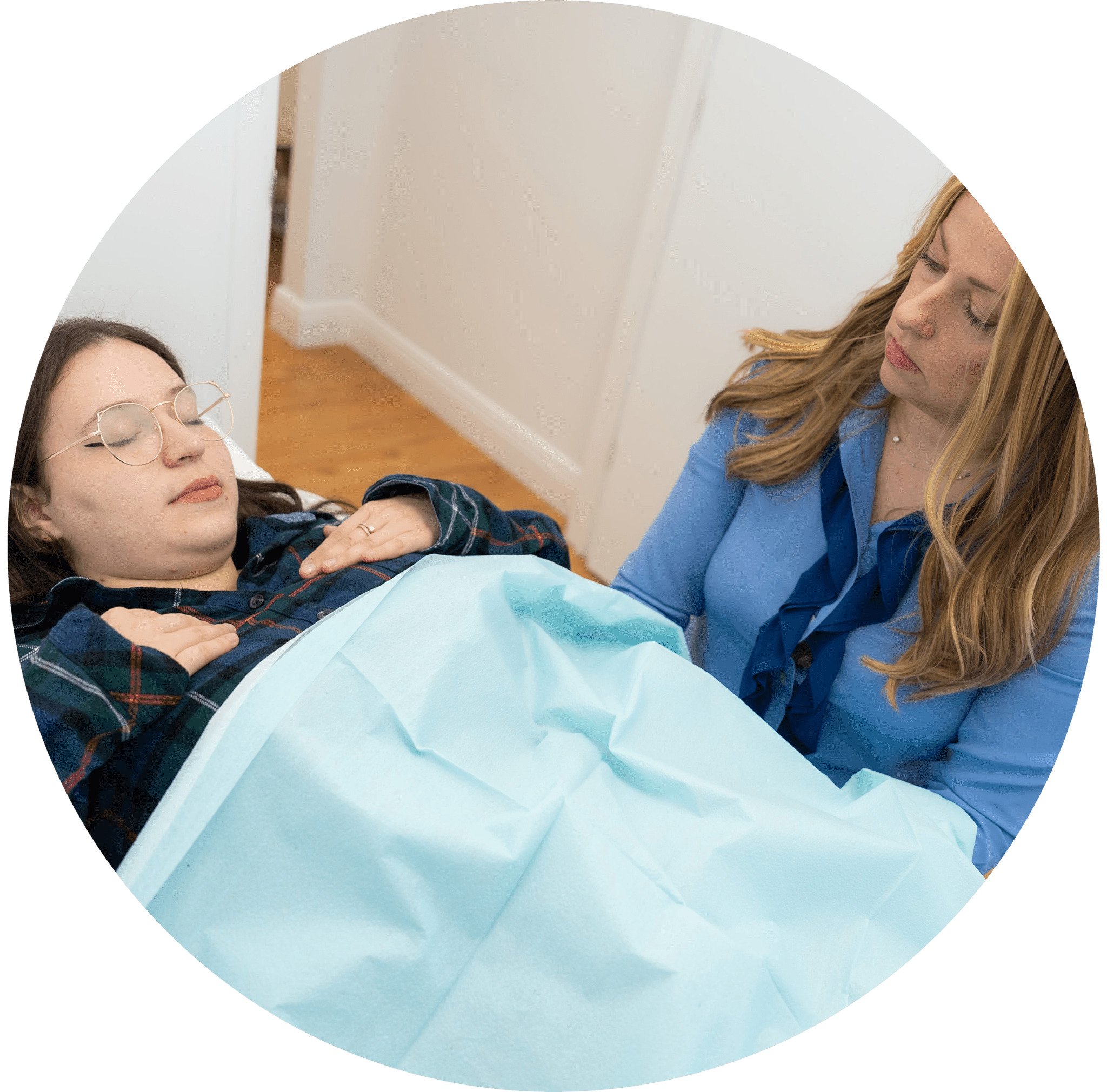 A woman in a blue blouse attentively discusses gut health with another woman, who is comfortably lying on a medical examination table covered with a light blue sheet.