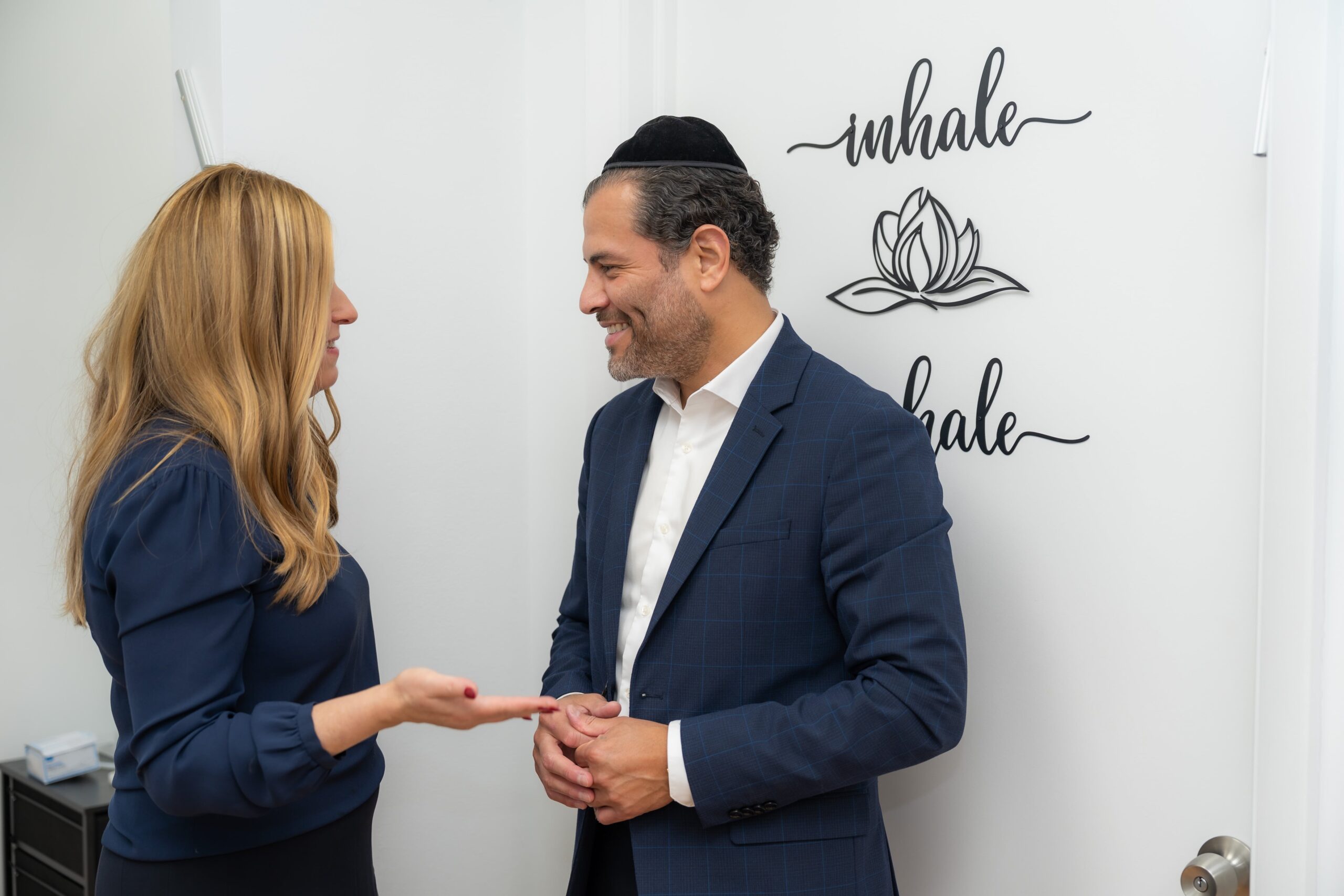 Two people are talking, with a wall sign in the background that reads 