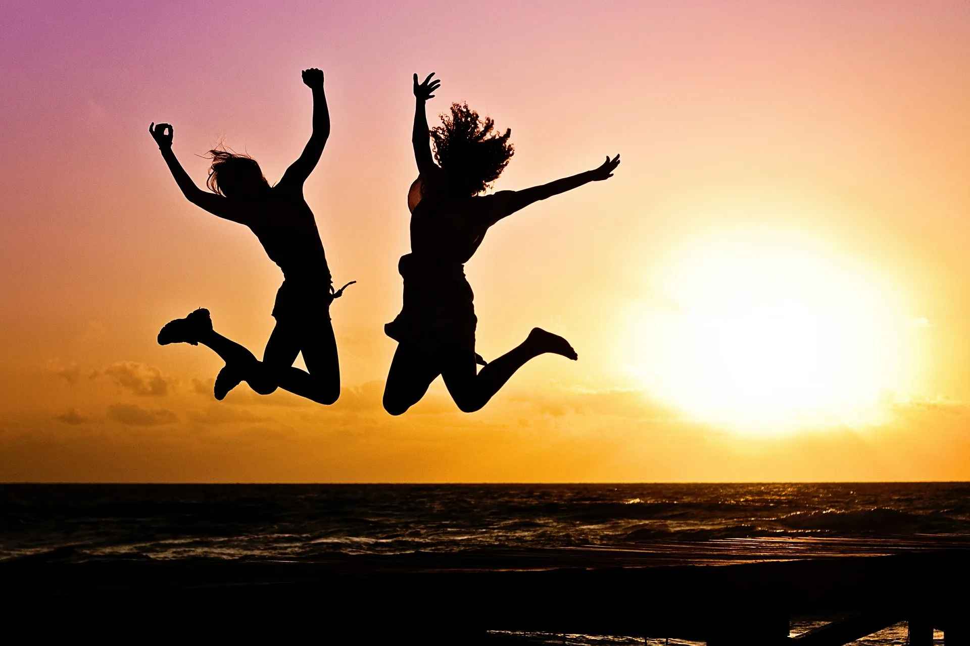 Two people are silhouetted as they joyfully jump into the air against a sunset backdrop by the ocean, celebrating their journey towards optimal gut health.