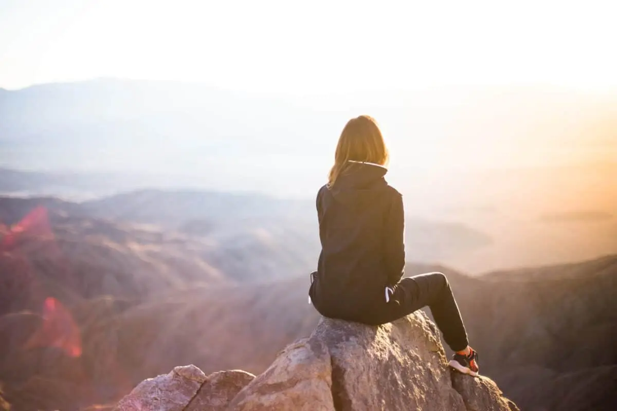 At sunrise, a person sits on a rock, taking in the breathtaking mountainous landscape. The gentle dawn light supports the body's natural hormonal rhythm, creating an ideal moment for nurturing gut health and overall well-being.